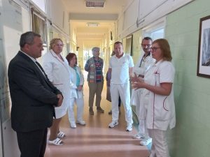 A képen a Tüdőgyógyászati osztály folyosóján, a kórtermek előtt hallgatja az ott dolgozó orvosok tájékoztatóját. Mellettük a püspököt kísérő kórházi vezetők állnak.